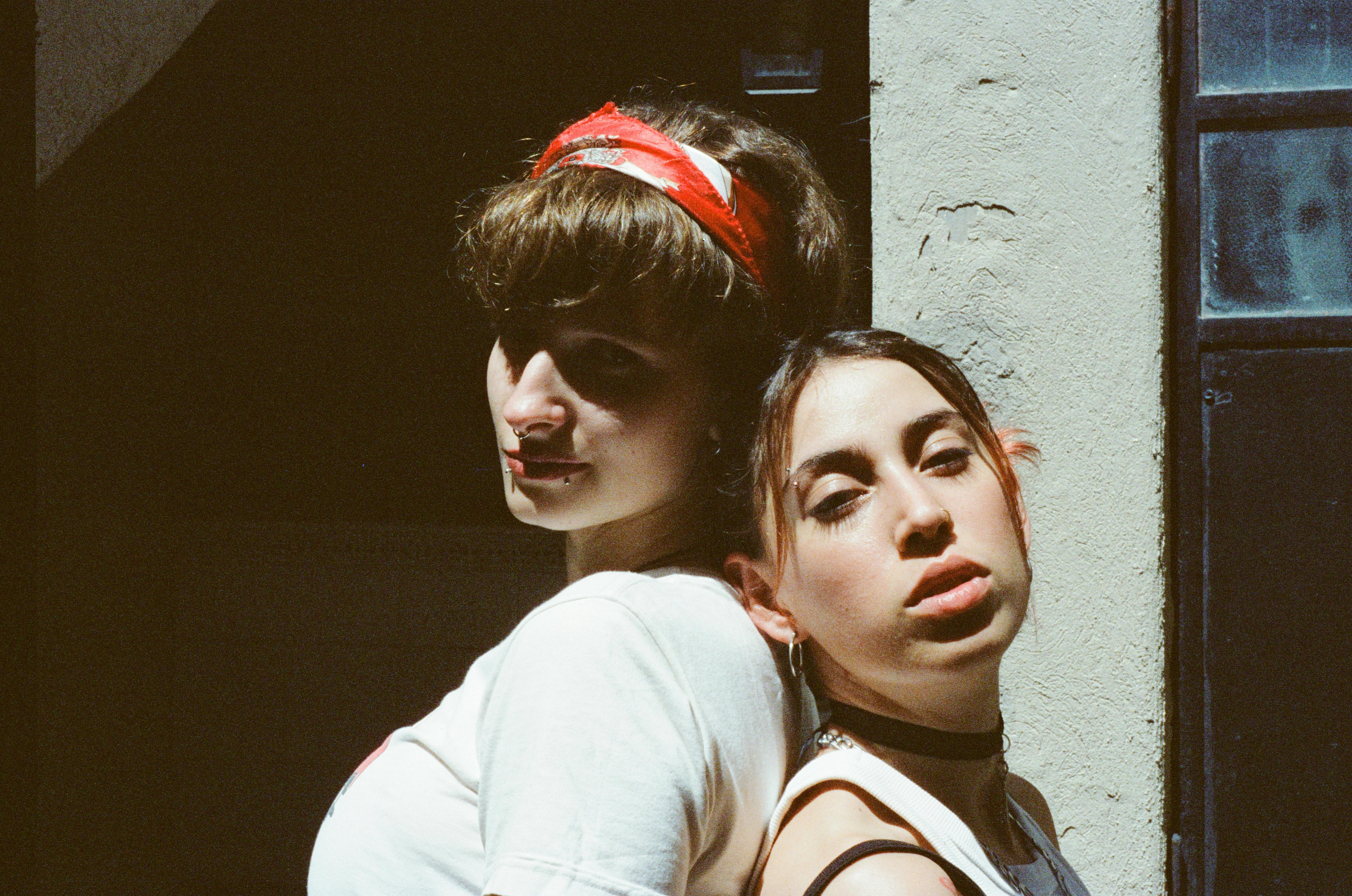 Kostnadsfria Stämningsfullt porträtt av två kvinnor som står nära varandra i stadsmiljö. Starkt solljus skapar dramatiska skuggor. Stock foto