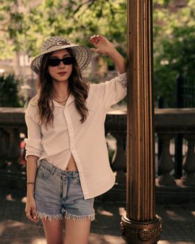 Fashionable young woman in sunglasses and sunhat posing outdoors during summer day.