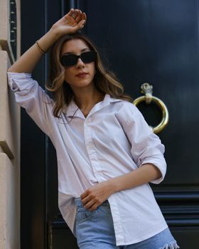 Fashionable woman in sunglasses poses against a stylish door with golden details.
