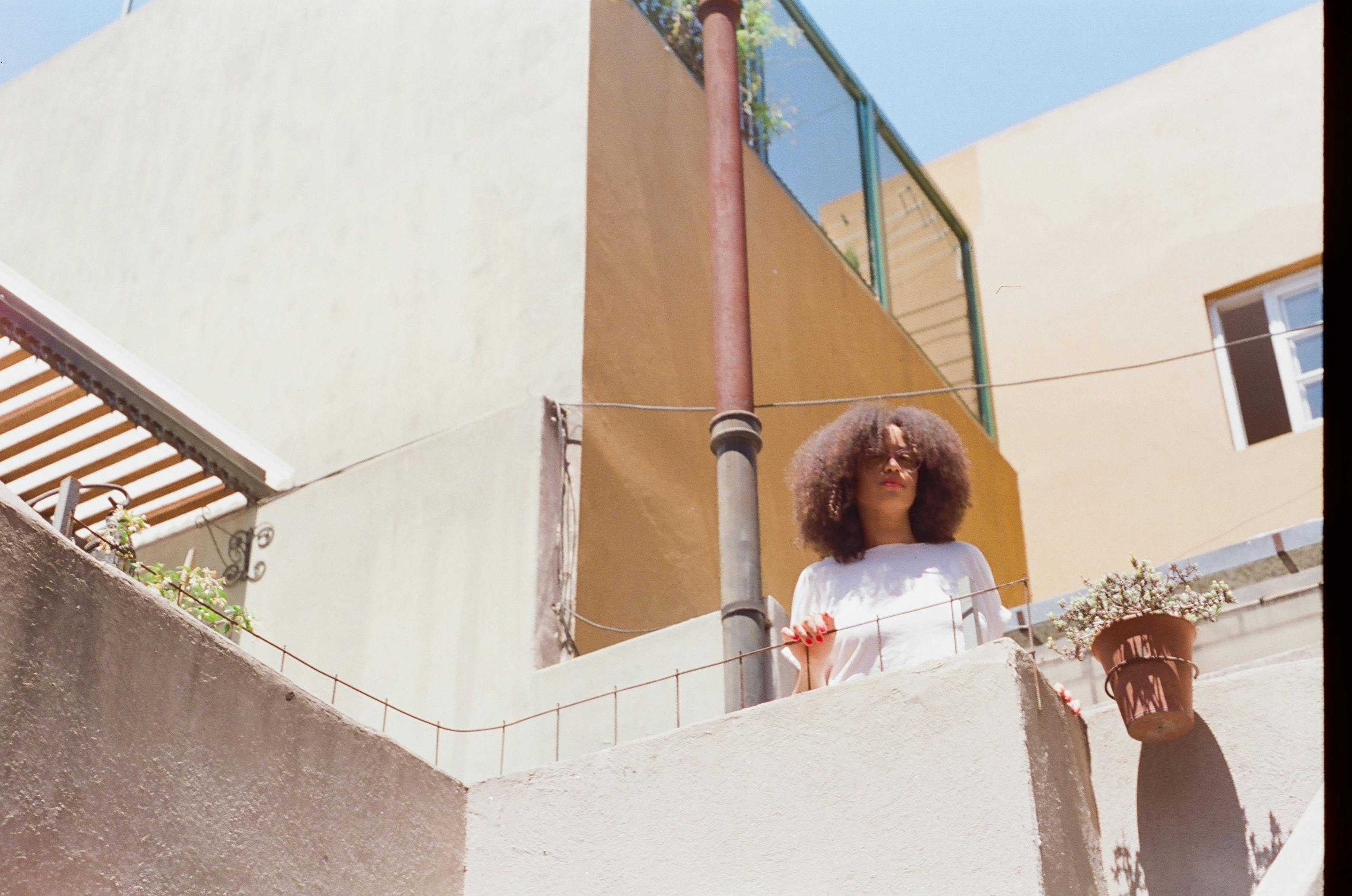 Kostnadsfria Kvinna njuter av solljus på ett tak, omgiven av stadsbyggnader och växter. Stock foto