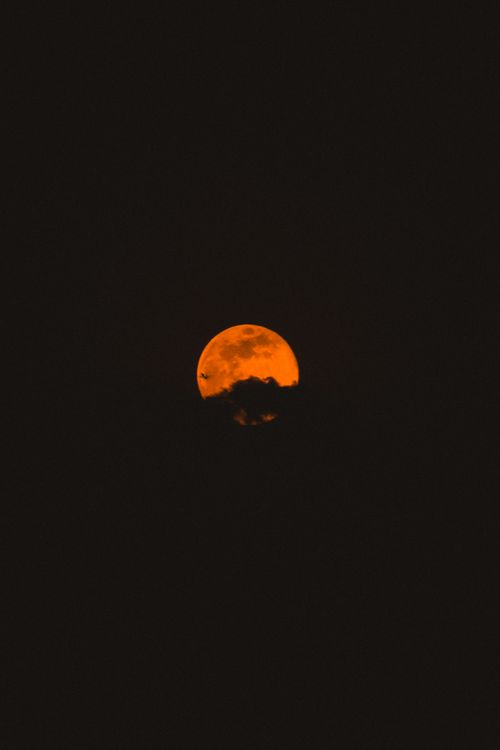 Free A stunning view of an orange moon rising through clouds against a dark night sky. Stock Photo