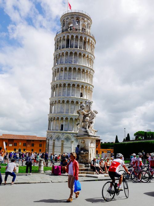 Free View of the Leaning Tower of Pisa with visitors and cyclists in the foreground, a popular landmark in Italy. Stock Photo
