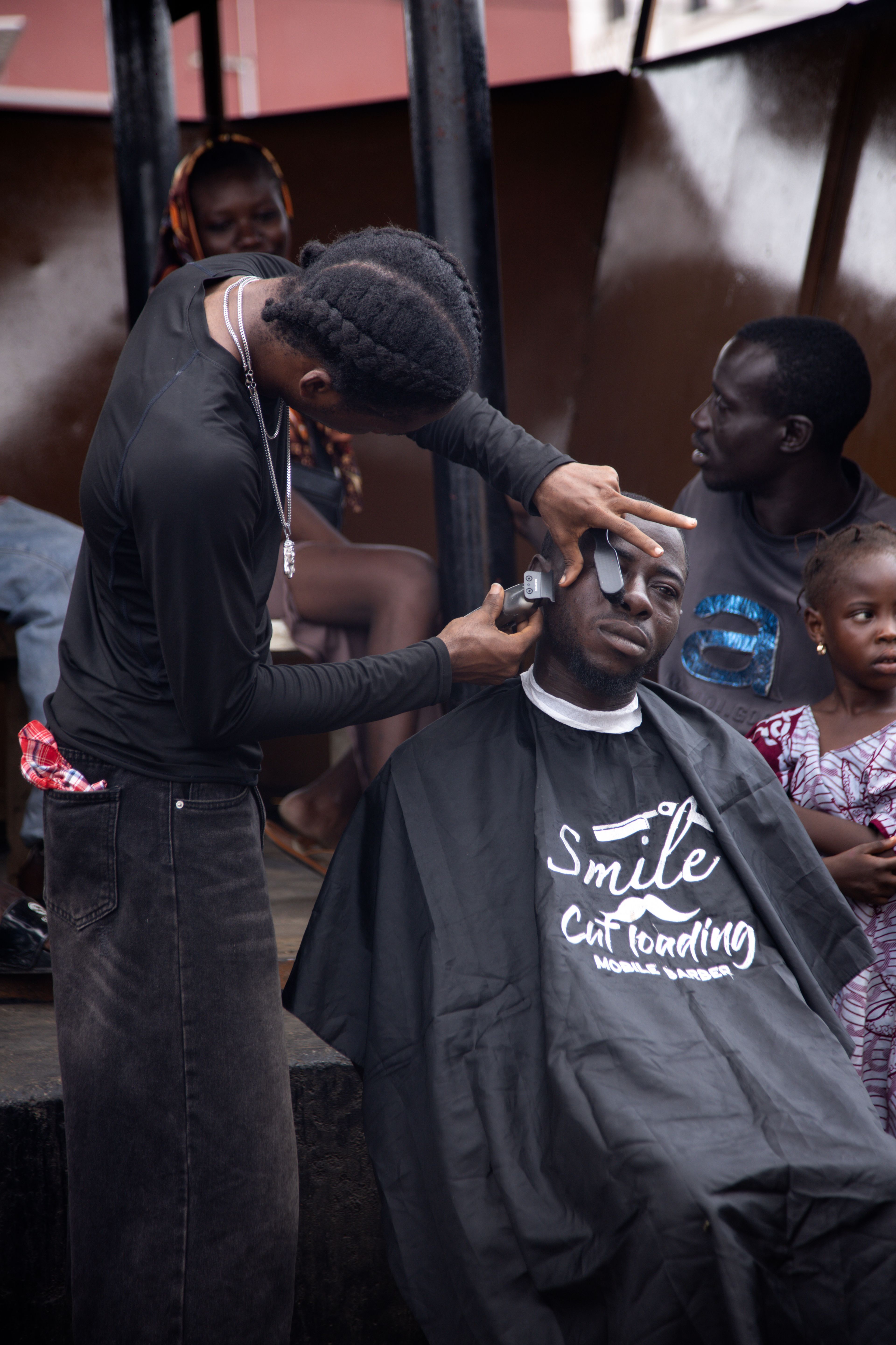 A barber cutting a customer’s hair at an outdoor barbershop