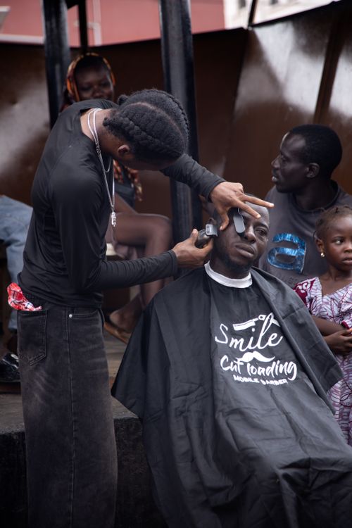 Free Outdoor barbershop with barber styling a man's hair while others wait. Stock Photo