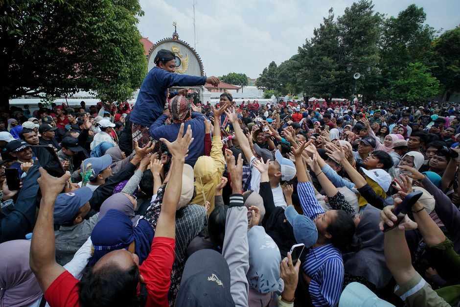 Large gathering at a traditional event in Yogyakarta, Indonesia, with people reaching up.