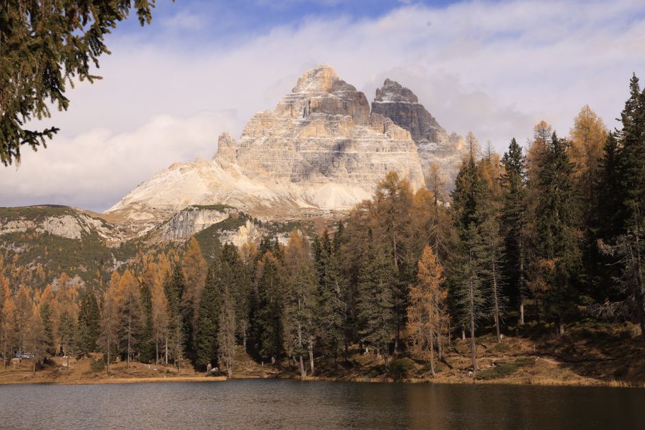 Majestic view of Tre Cime di Lavaredo with autumn trees by the lake.