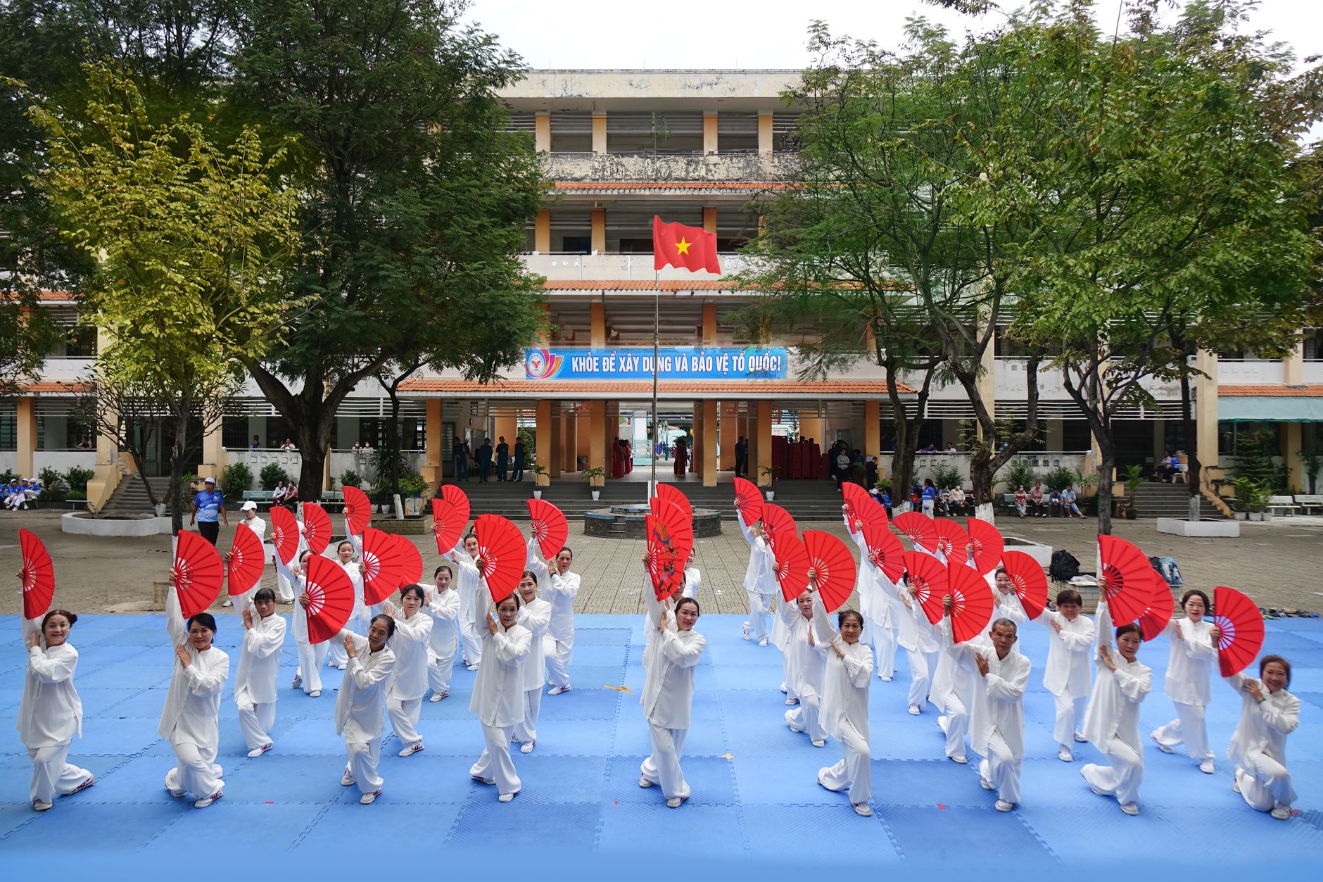 A group of adults performing a traditional fan dance in white attire outdoors.