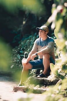 A young man in casual attire relaxes with a drink in a sunlit park setting.