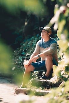 Casual man sitting outdoors with a drink, enjoying a sunny day in the park.