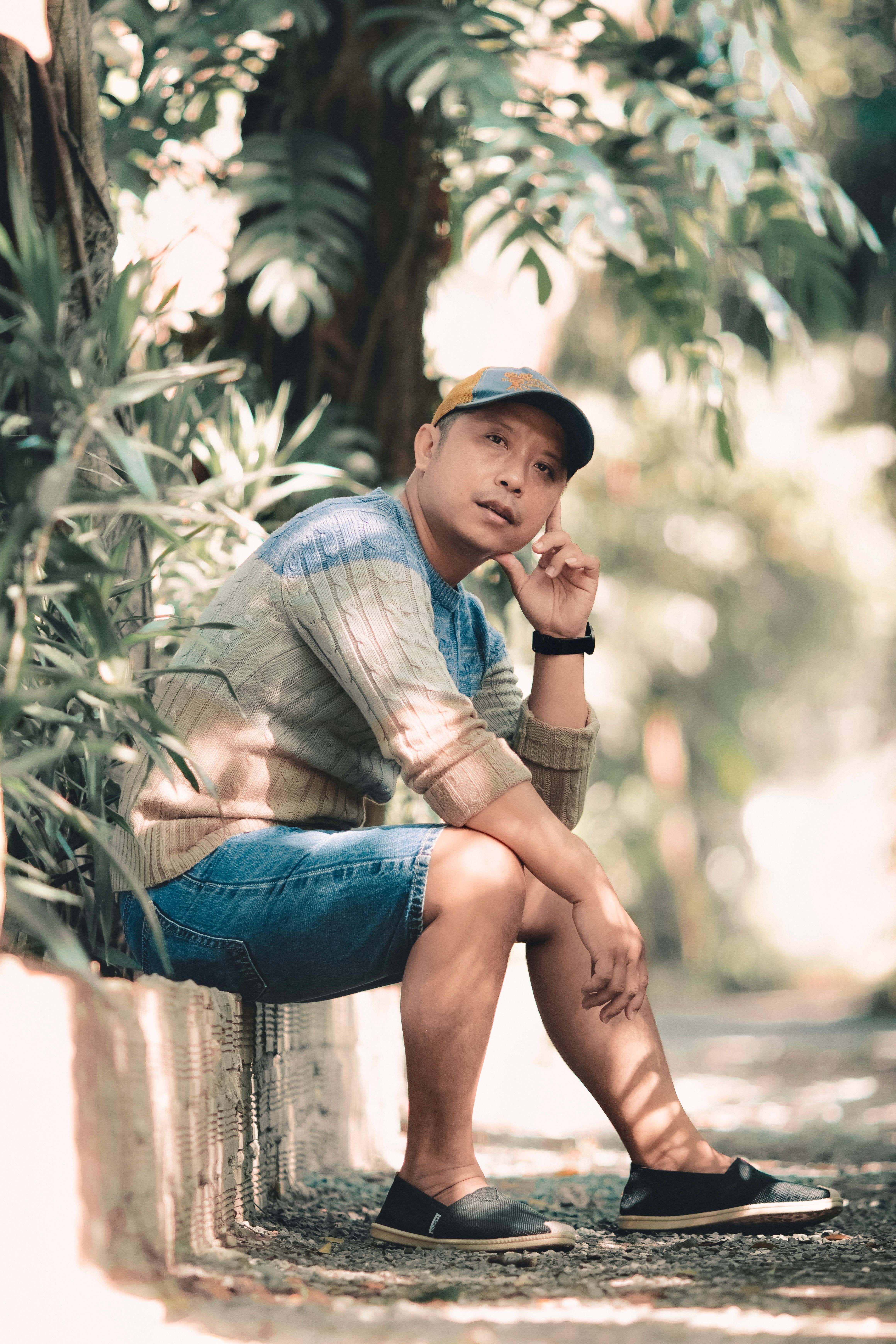 Man sitting on a wall outdoors in a natural setting, wearing casual attire.