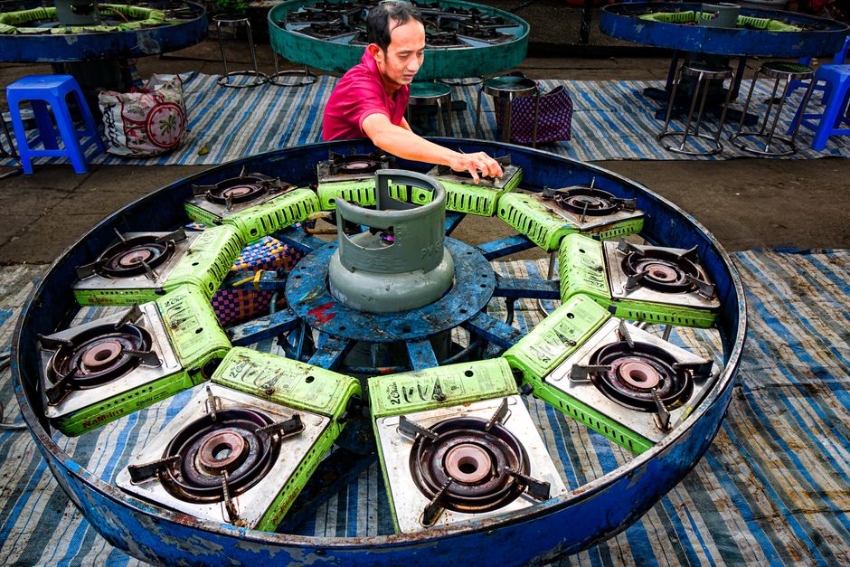 A man arranges stove burners around a central gas cylinder outdoors.