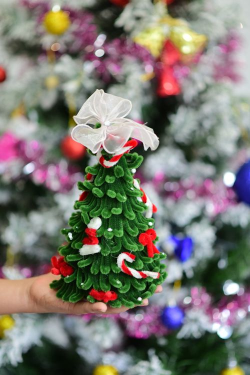 Free Close-up of a hand holding a festive mini Christmas tree against a blurred colorful background. Stock Photo
