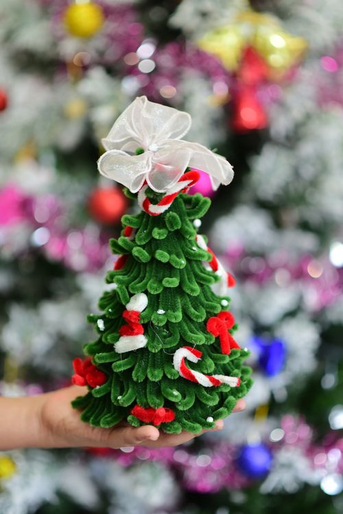 Free Hand holding a decorated mini Christmas tree with a blurred festive background. Stock Photo