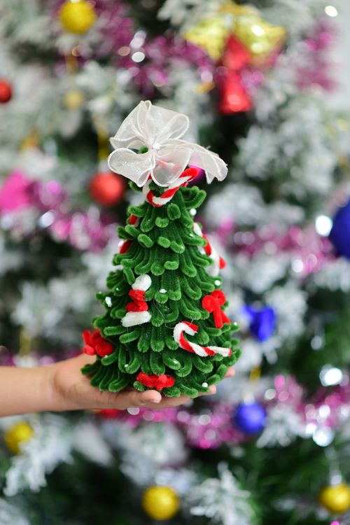 Free A hand holds a small ornamental Christmas tree with a festive background. Stock Photo
