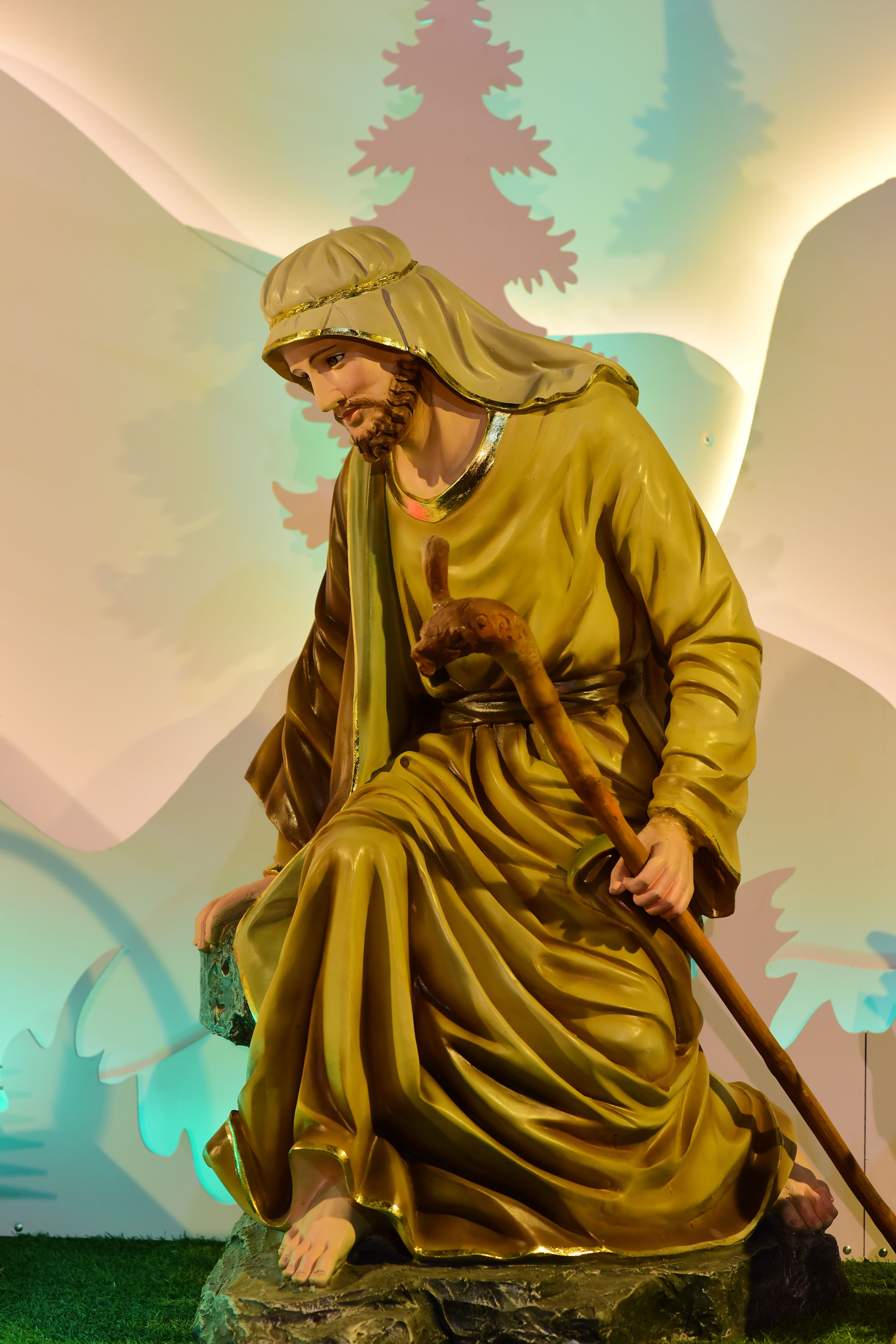 Statue of a shepherd holding a staff, illuminated by colorful lights, indoors.