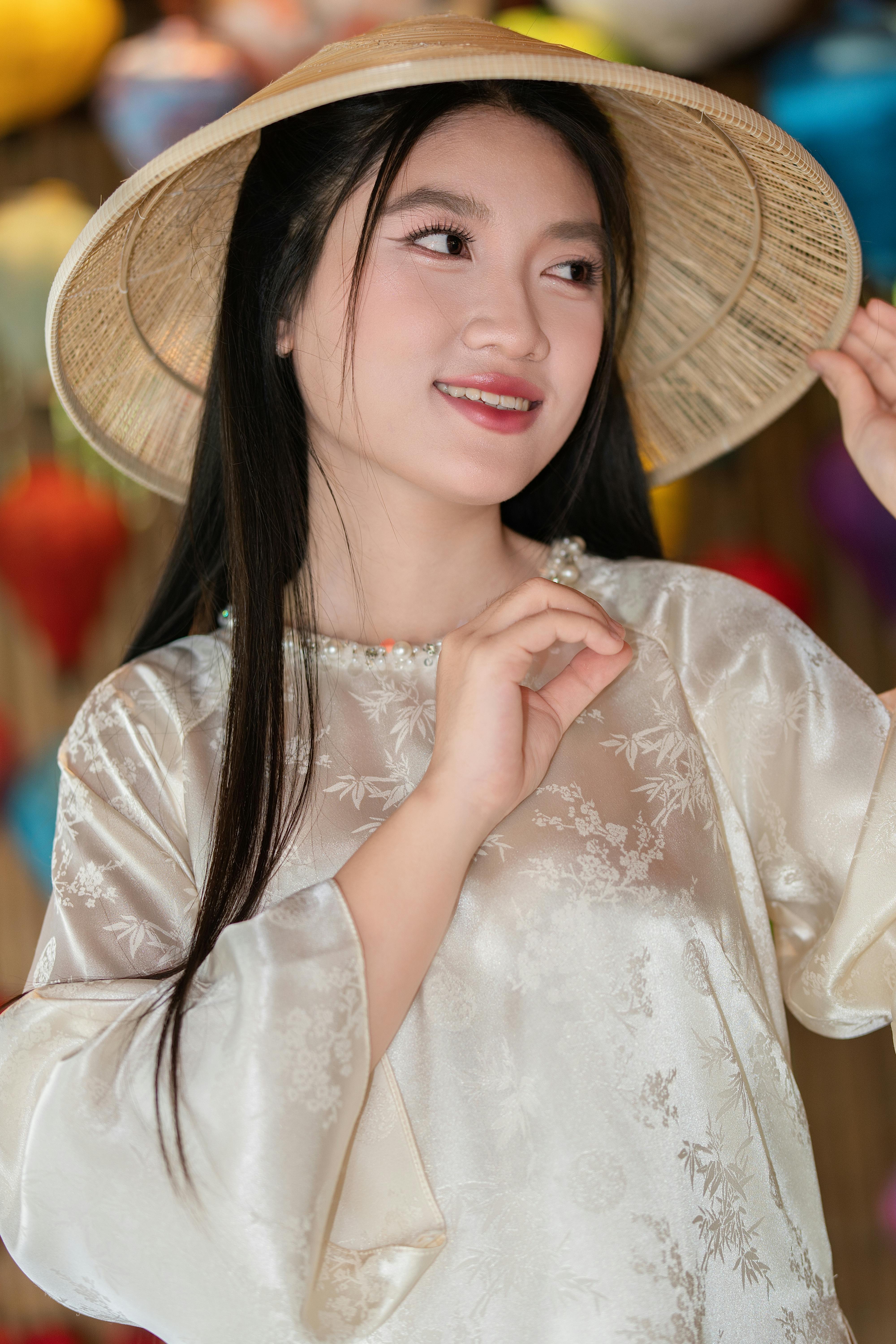 Young woman in beautiful Asian dress and hat smiling gently.