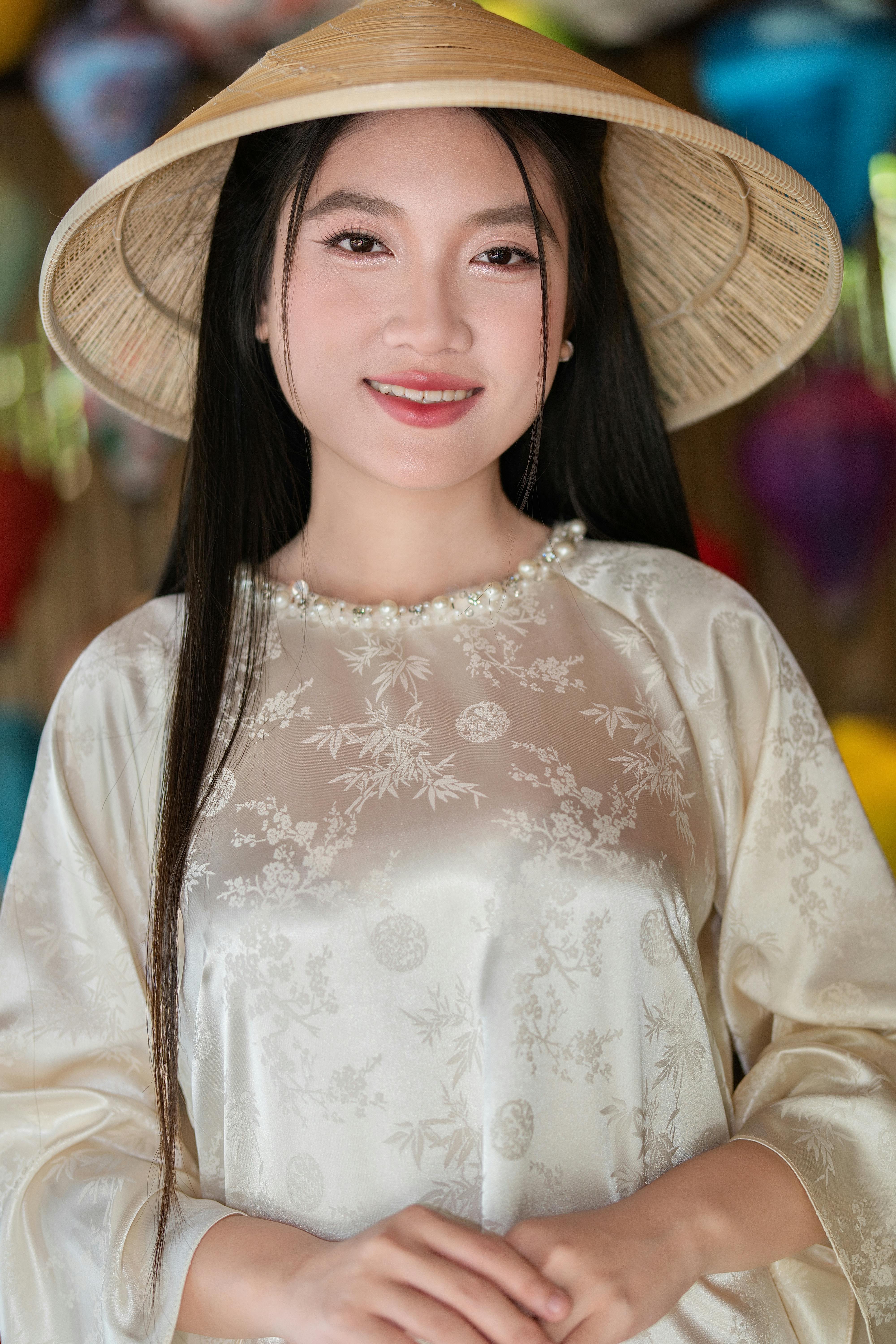 Smiling woman in elegant traditional Vietnamese dress and conical hat.
