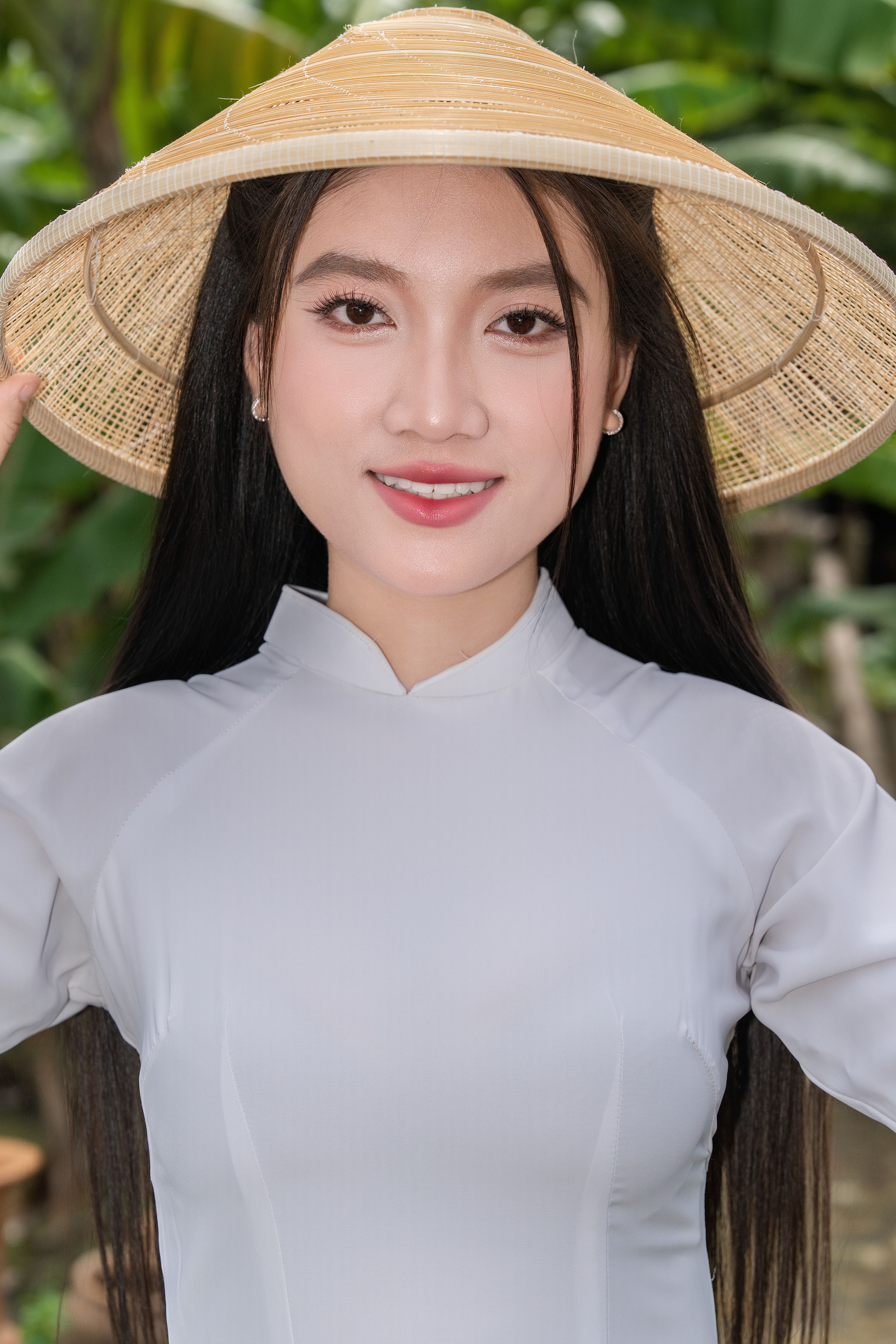 Portrait of a young woman wearing a traditional Vietnamese conical hat outdoors.