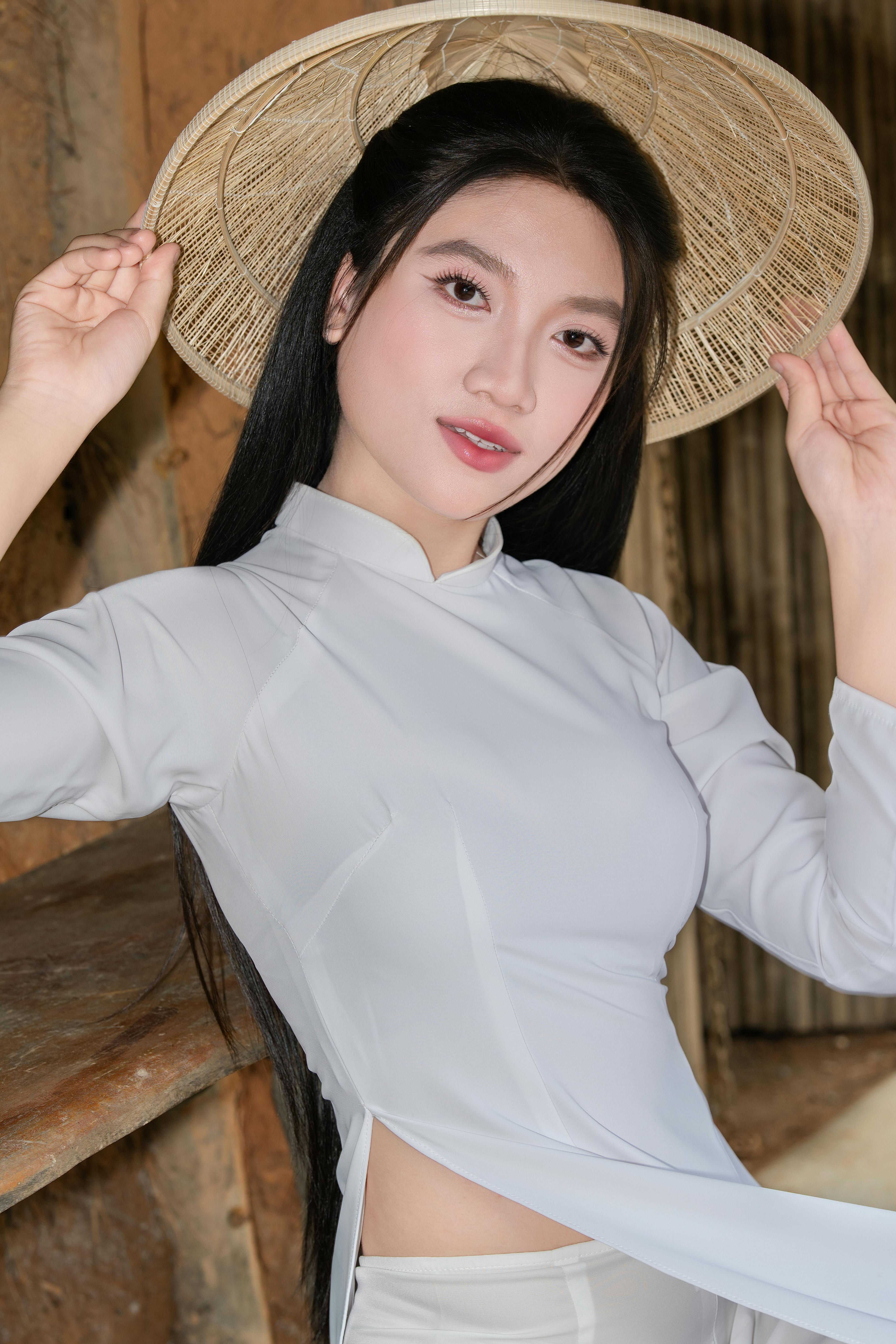 Young woman in traditional dress holding a hat, posing elegantly indoors.