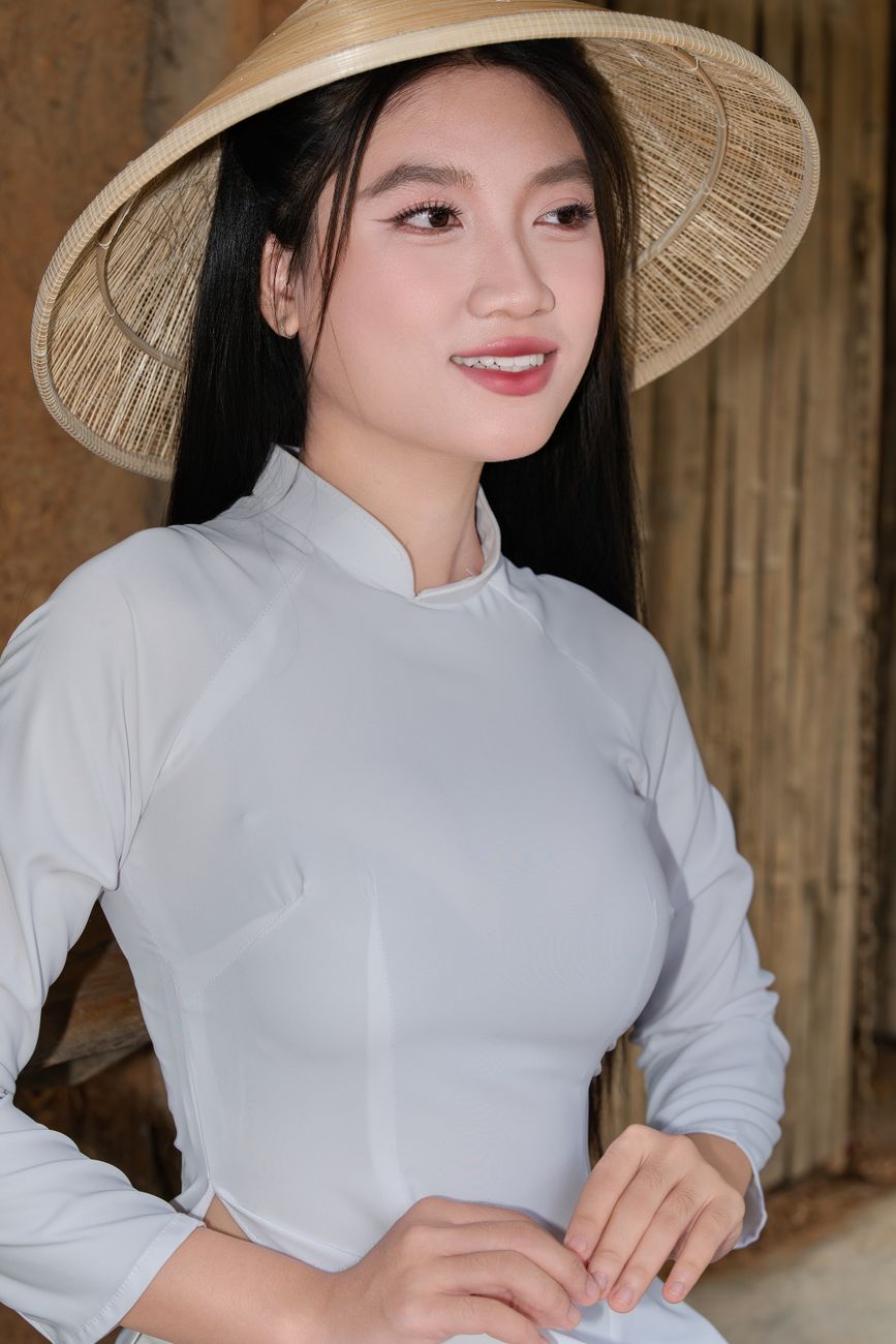 Smiling woman in Vietnamese dress with a conical hat outdoors.