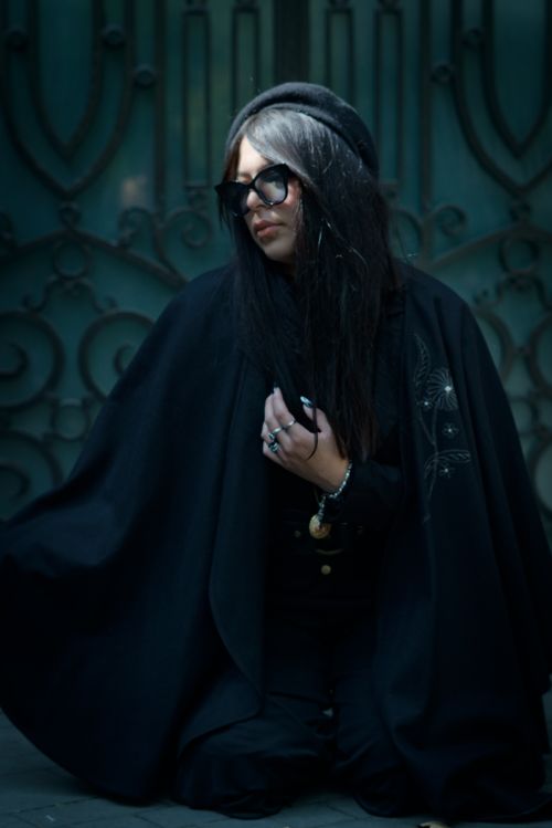 Free A stylish woman in sunglasses wearing a black coat kneels in front of ornate doors. Stock Photo