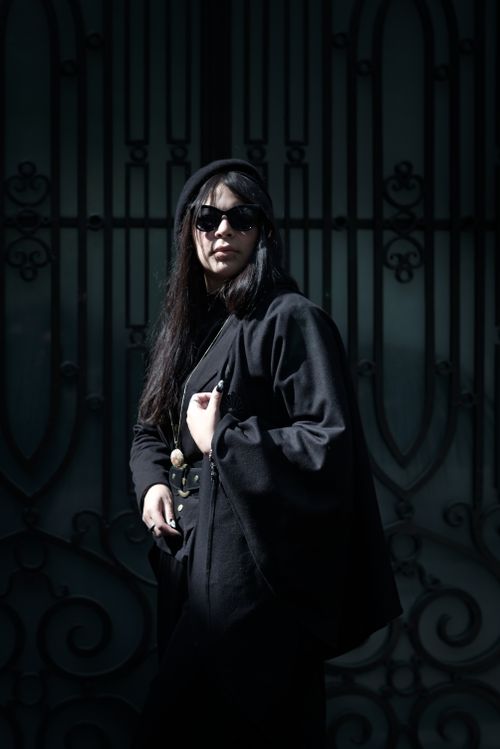 Free Fashionable woman in black attire and sunglasses posed against a decorative gate. Stock Photo