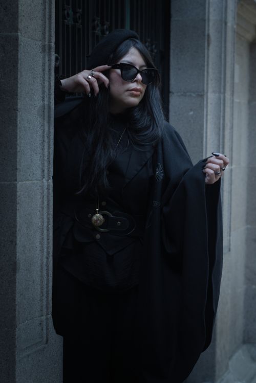 Free A stylish Latina woman wearing sunglasses and dark attire confidently leans against a stone wall. Stock Photo
