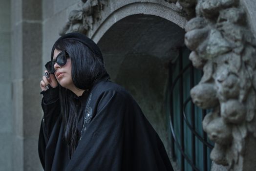 Woman in dark gothic clothing posing by intricate stone architecture in Mexico City.