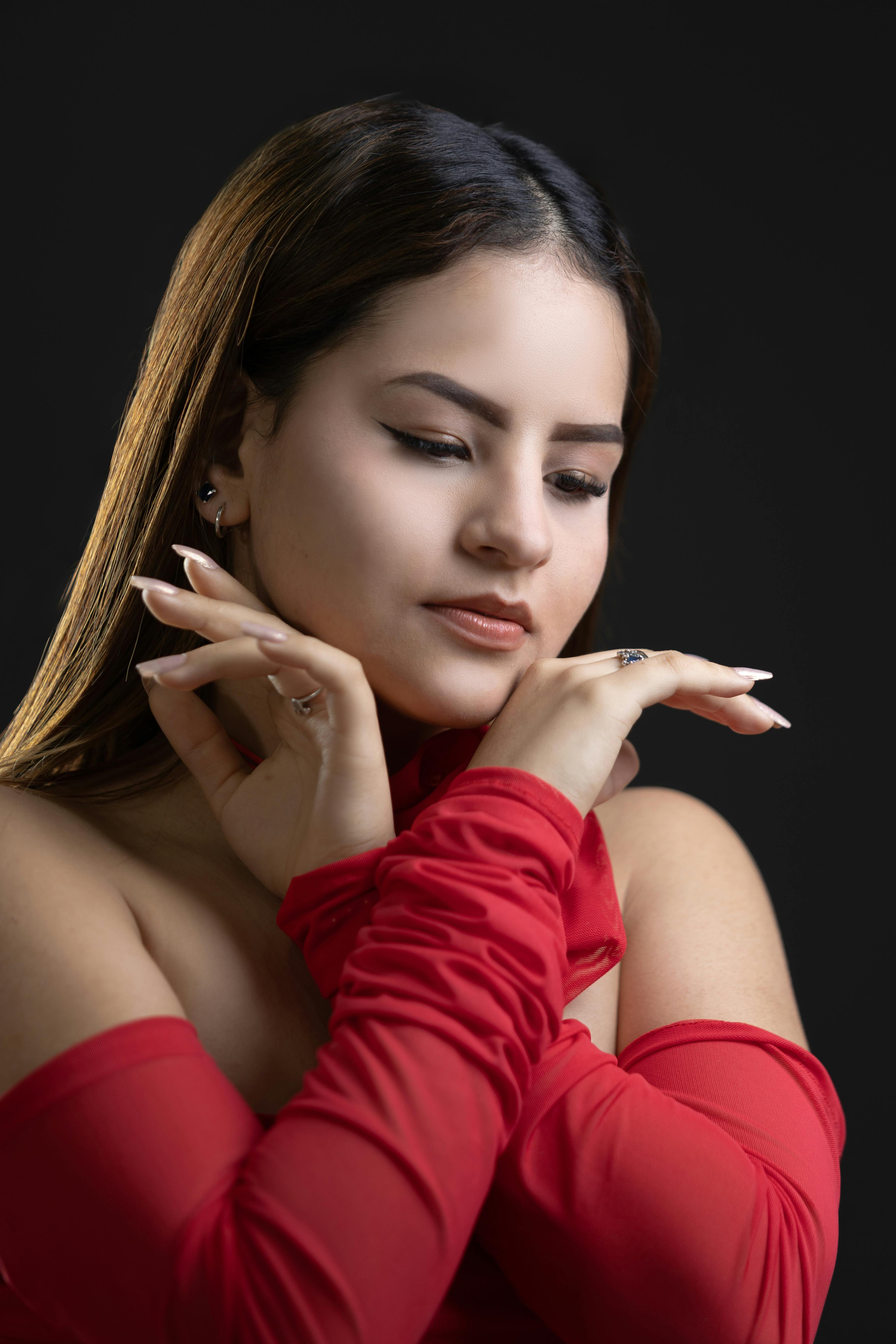 grátis Retrato artístico de uma mulher com as mãos juntas em um vestido vermelho sobre um fundo escuro. Foto profissional