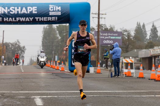Athlete running in a marathon race under a halfway banner on a cloudy day.