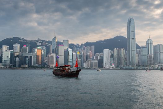 Scenic view of a traditional junk boat sailing in Victoria Harbour with Hong Kong skyline in the background.