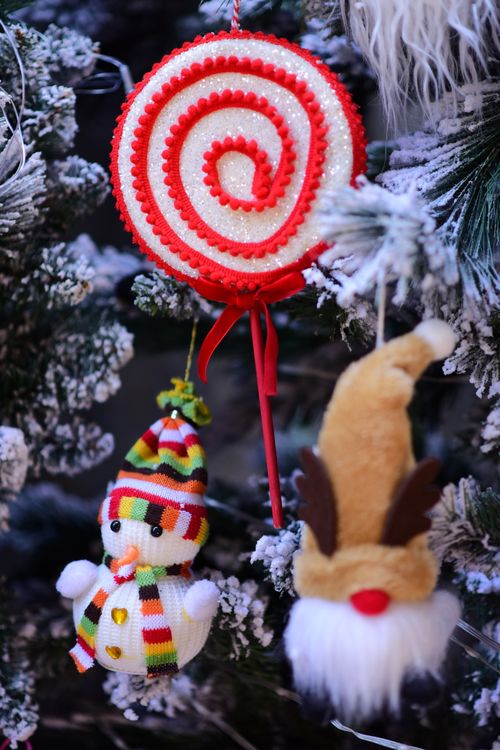 Free Cozy Christmas decorations hanging on a snowy tree branch, including a swirl ornament, snowman, and reindeer toy. Stock Photo