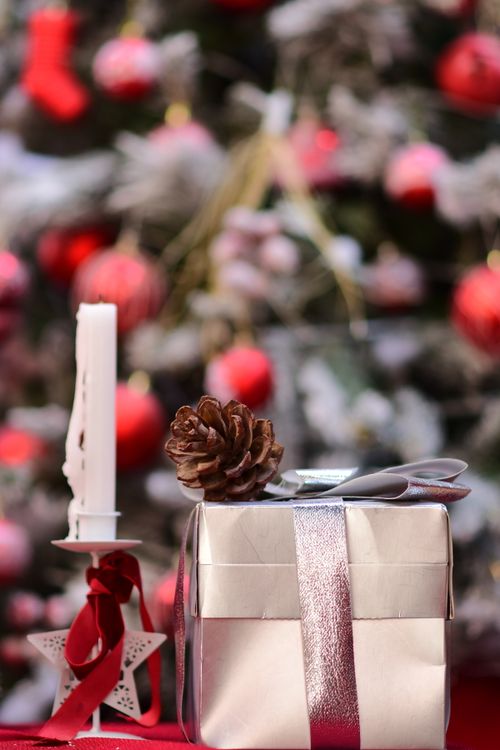 Free A silver gift box and candle with a pinecone in front of a decorated Christmas tree. Stock Photo