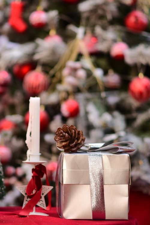 Free A close-up of a wrapped gift with a pinecone on top beside a candle and Christmas tree. Stock Photo