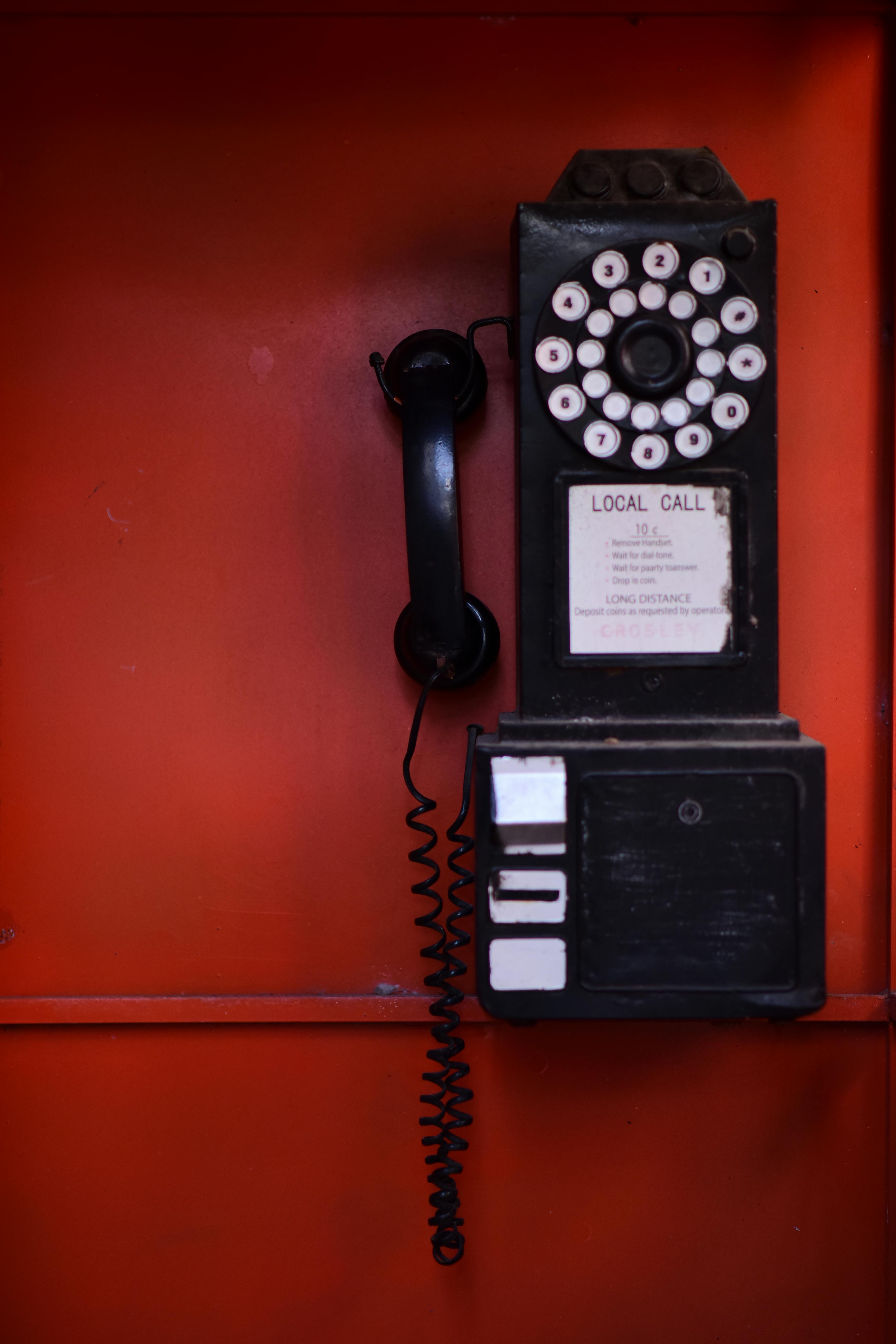 Kostenlos Ein rustikales Münzfernsprecher mit Wählscheibe an einer leuchtend orangefarbenen Wand. Ein nostalgischer Blick in die Geschichte der Kommunikation. Stock-Foto