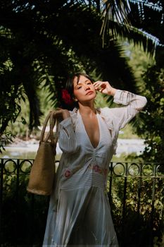 An elegant woman in a flowing dress poses gracefully under lush greenery in Mexico City.