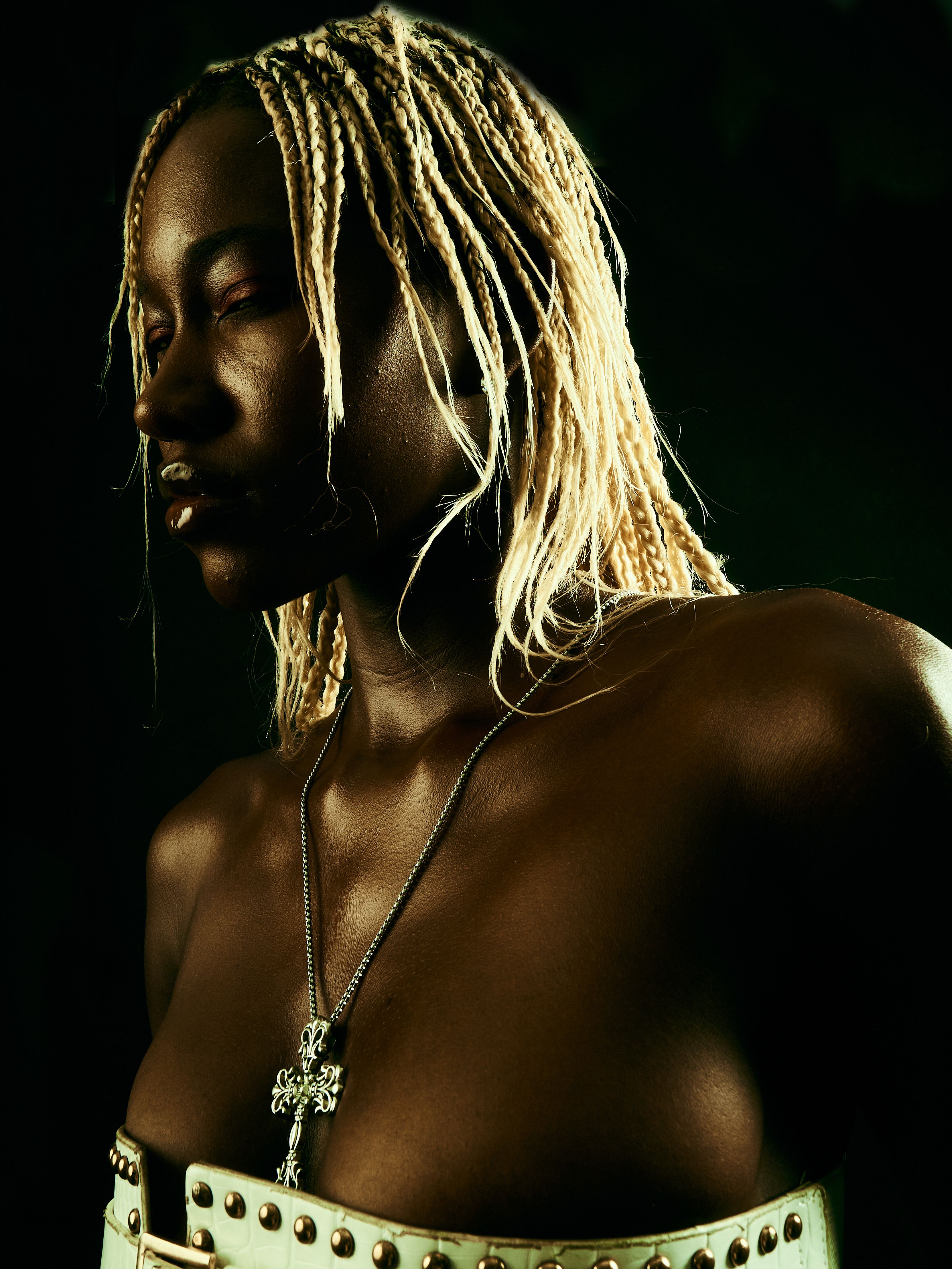 Moody portrait of a woman with blonde braids wearing a necklace, in low light.