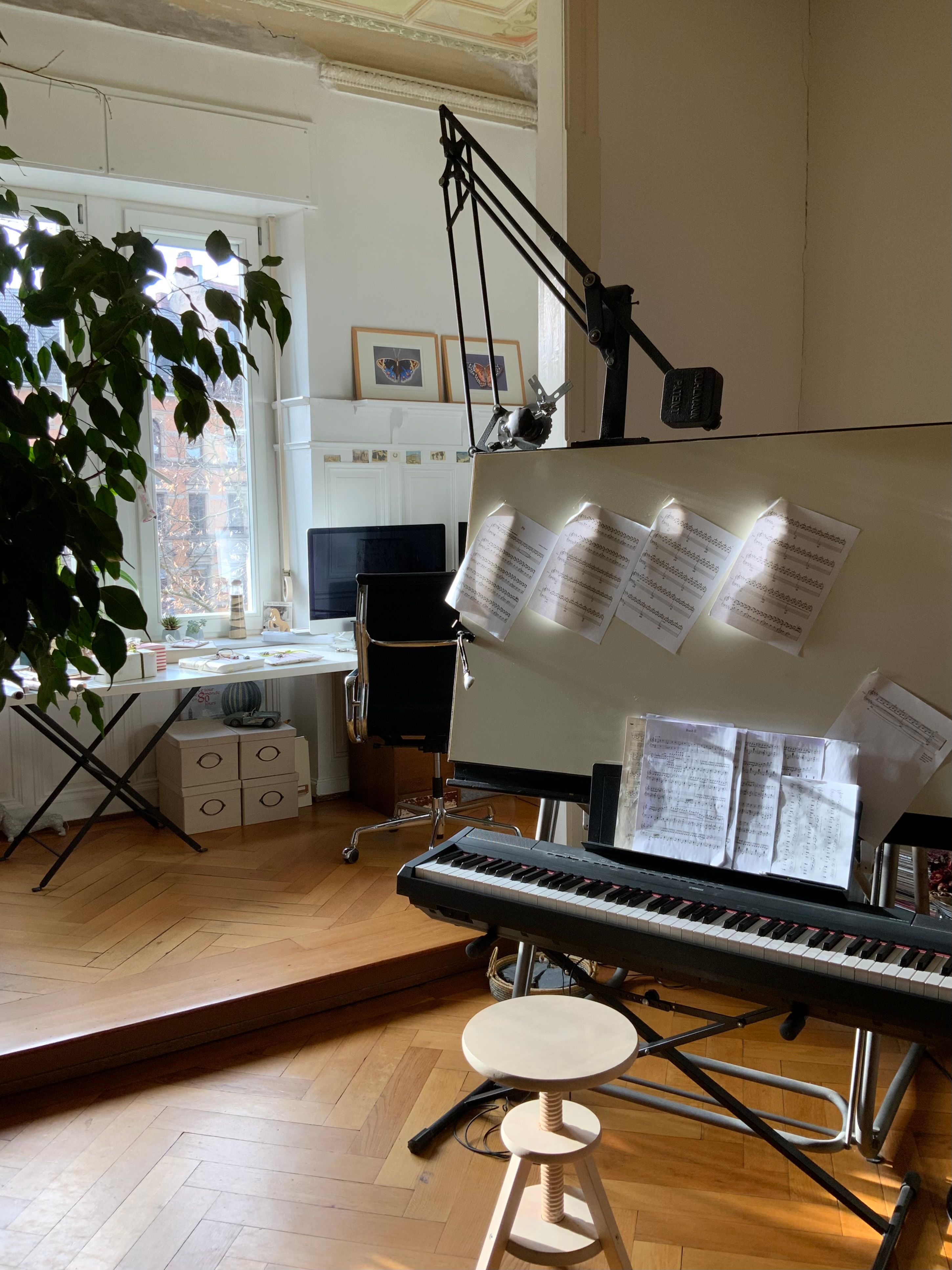 A well-lit music room with keyboard, sheet music, and study area by a large window.