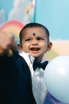 Smiling baby boy on his first birthday with a colorful backdrop and balloon.