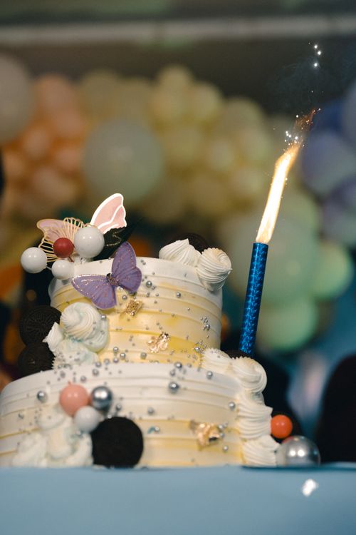 Free Colorful two-tier birthday cake with decorations and a lit candle, perfect for celebrations. Stock Photo