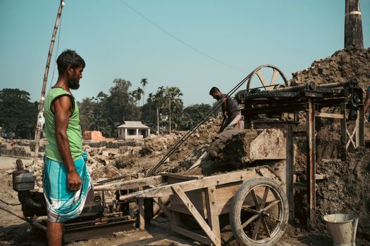 Two men working at a rural brick kiln in South Asia under a clear sky.