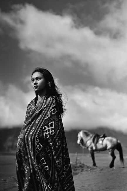 Striking black and white photo of a woman in traditional clothing with a horse in a scenic outdoor setting.