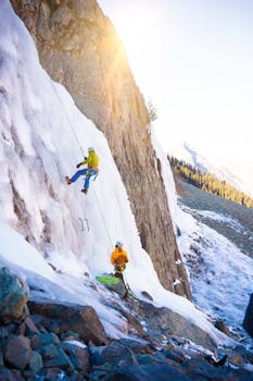 Two climbers ice climbing a mountain during sunrise, showcasing adventure and teamwork.