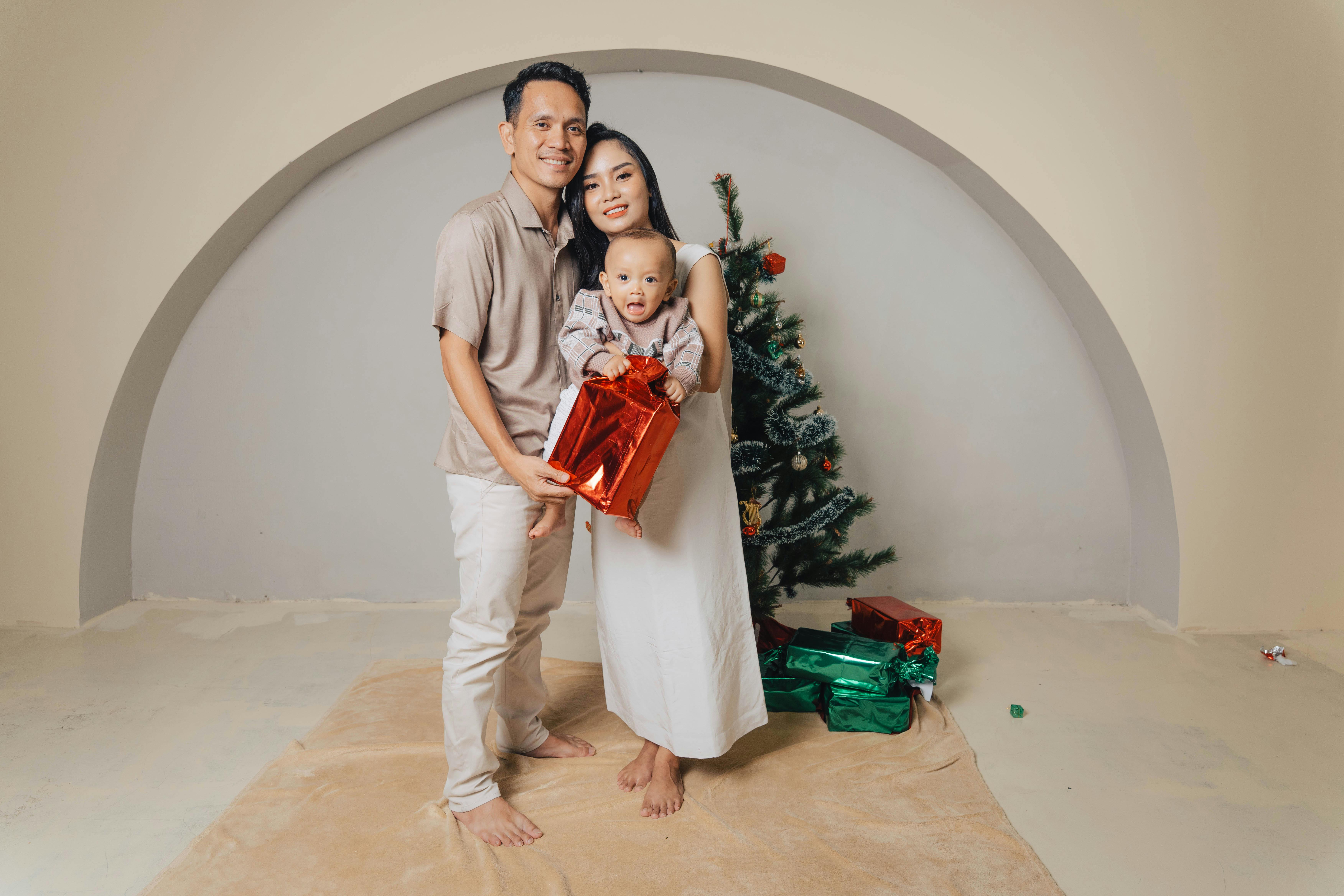 Happy family with a baby celebrating Christmas near a decorated tree with gifts.