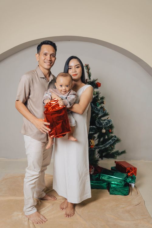 Free Warm family portrait beside a Christmas tree holding colorful gift boxes, spreading festive cheer. Stock Photo