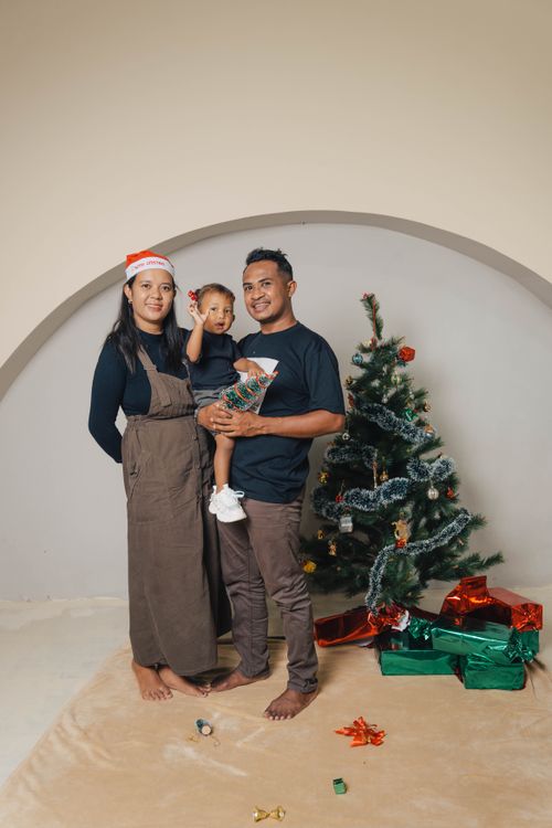 Free Happy family posing with a Christmas tree and festive gifts indoors. Stock Photo