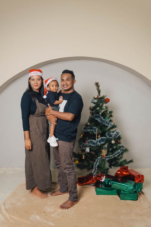 Free Smiling family in festive attire gathered around a decorated Christmas tree with presents. Stock Photo