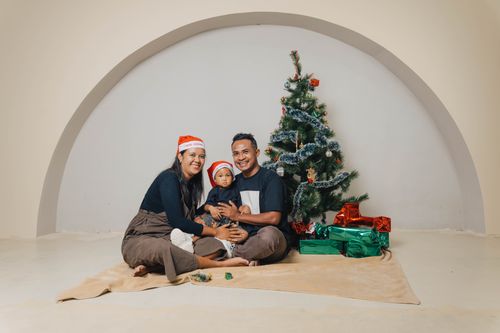 Free A joyful family sitting by a decorated Christmas tree with gifts, celebrating the festive season. Stock Photo