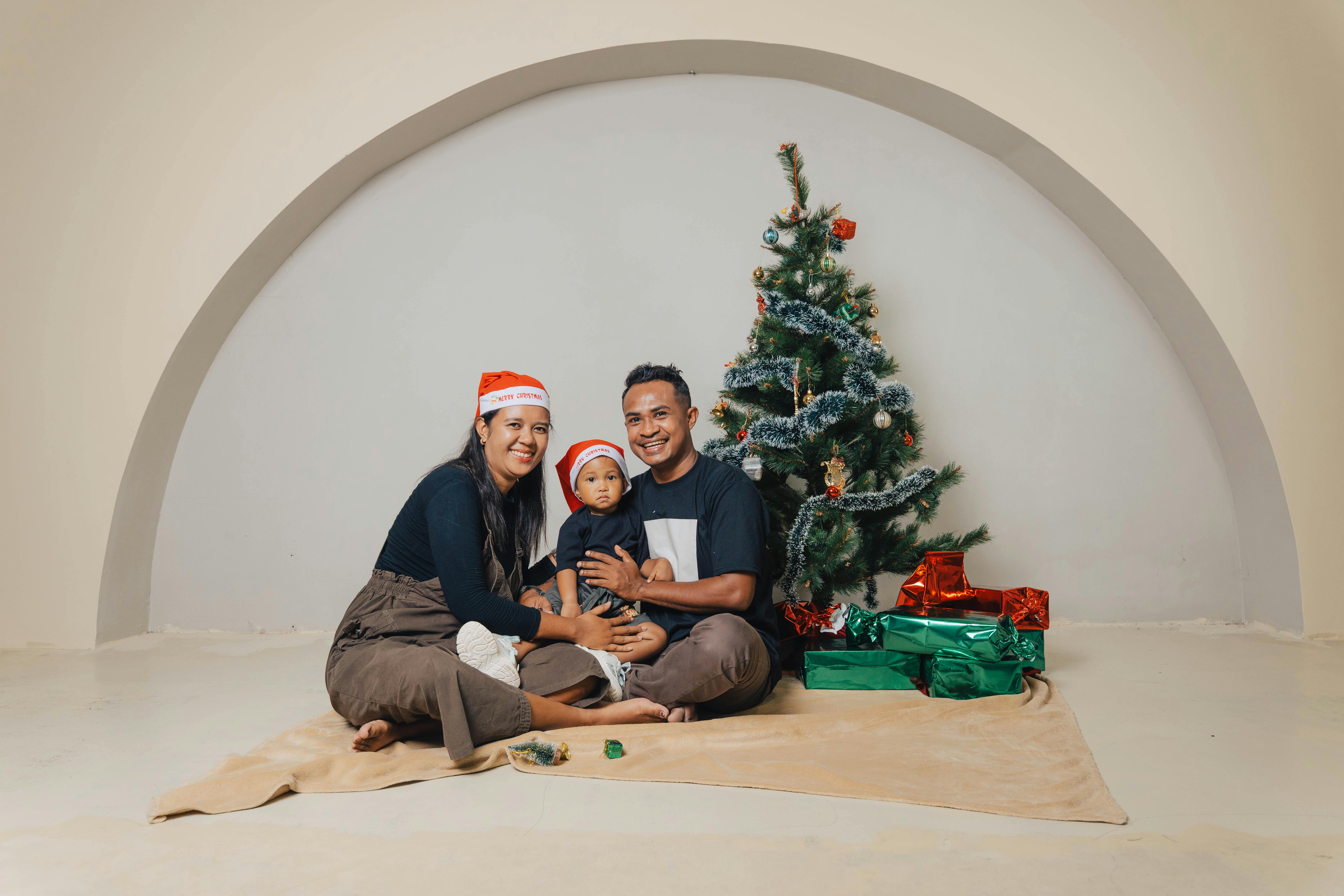 ฟรี ครอบครัวยิ้มแย้มแจ่มใสกับต้นคริสต์มาสและของขวัญ เพลิดเพลินกับวันหยุดภายในบ้าน คลังภาพถ่าย