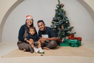 Happy family posing by a Christmas tree with gifts, embracing holiday spirit.